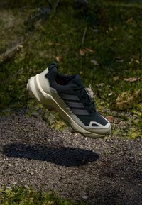 Czarne i oliwkowo-zielone buty sportowe z teksturowaną cholewką, trzema jasnoszarymi paskami oraz wzmocnioną podeszwą. Zaprojektowane z myślą o użytku na świeżym powietrzu.