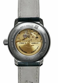 Edelstahl-Uhrboden mit Glasscheibe, die ein goldenes mechanisches Uhrwerk zeigt, mit graviertem Text und einem beigen Lederarmband.