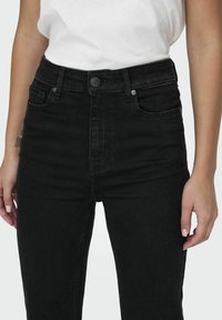 Svarta högmidjade jeans med knäppning, framfickor och en slät denimtextur. Designen är skräddarsydd och välanpassad.