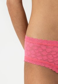 Rosa spetsunderkläder med ett blommönster, vågiga kanter och ett mjukt elastiskt midjeband som framhäver textur och detaljer.