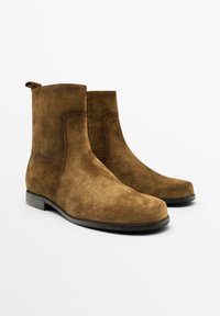 Braune Wildleder-Ankle Boots mit glatter Oberfläche, abgerundeter Zehenpartie und einem leichten Absatz. Verfügt über eine Zuglasche für ein einfaches Anziehen.