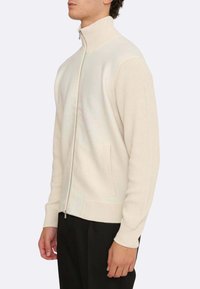 Helle beige Zip-Pullover mit einem gerippten Kragen und Bündchen. Verfügt über einen kontrastierenden strukturierten Strick an den Ärmeln und seitlichen Taschen.