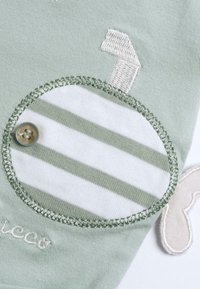 Tissu vert menthe avec un patch circulaire blanc comportant des rayures vertes et un bouton. Comprend des accents brodés et des détails en application.