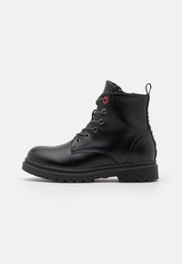 Black leather ankle boots with a round toe, textured finish, lace-up front, red eyelet accents, and a textured rubber sole.