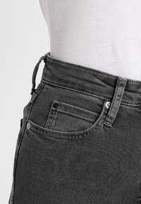 Jeans de mezclilla gris con una cintura alta, diseño tradicional de cinco bolsillos y un patrón de costura distintivo a lo largo de la cinturilla.