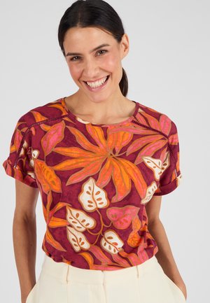 Top a maniche corte di color cremisi con un vivace motivo floreale in arancione, rosa e crema. Il tessuto appare morbido, con maniche arrotolate e scollo a girocollo.