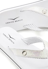 Balti šlepetės su taškeliais dekoruotais dirželiais ir tekstūruotu akcentu. Įrengtos sidabrinės detalės ir „Venice Beach“ prekės ženklo logotipas ant pado.