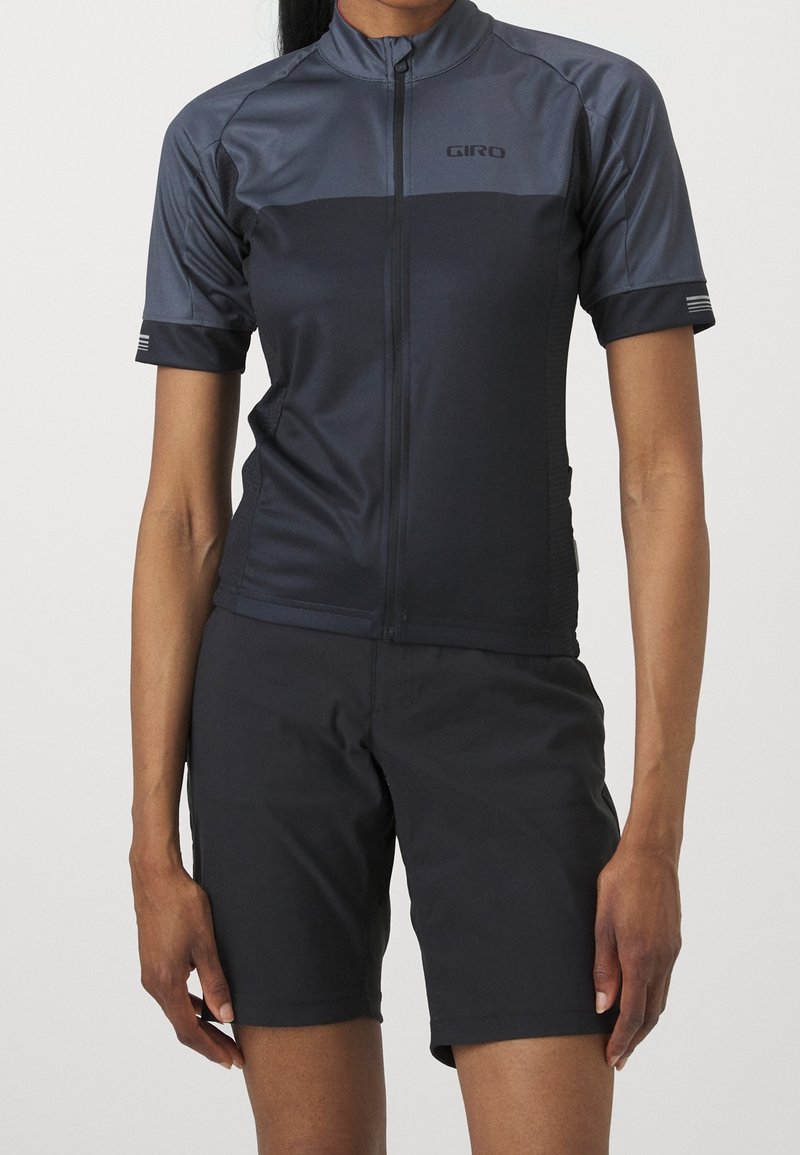 Kortärmad cykeltröja i mörkgrått med dragkedja framtill och logotyp. Matchas med svarta shorts. Slät, elastisk tyg, åtsittande design.