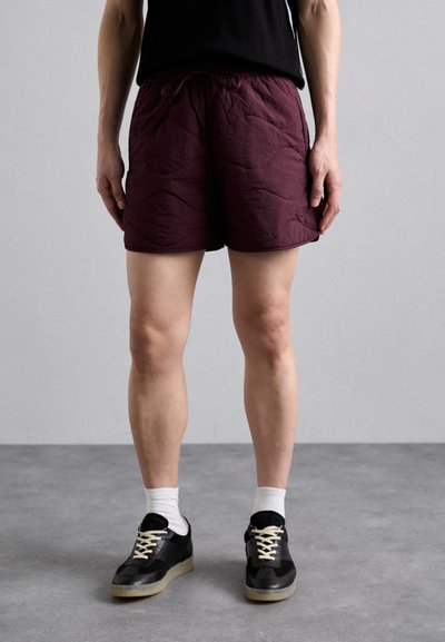 Pantaloni scurți bordeaux cu o suprafață texturată, talie elastică și șnur de ajustare. Asortați cu adidași negri și șosete albe până la glezne.