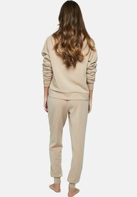 Beige hoodie en jogger set gemaakt van zachte stof. Kap aan de achterkant, ribgebreide manchetten, ontspannen pasvorm en taps toelopende broek met elastische enkels.