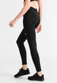 Svarta träningsleggings med hög midja, slät textur och en subtil Nike-logga på sidan. Bärs med svarta sneakers.