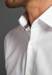 Camicia bianca con tessuto testurizzato. Presenta un colletto foderato con un motivo a contrasto bianco e nero e bottoni perlacei.