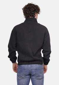 Giubbotto bomber nero con colletto alto, polsini e orlo elasticizzati. Tessuto morbido e design minimale, indossato con jeans blu.