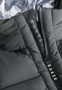 Close-up of a black padded jacket with a partially open zipper featuring a pull tab labeled "BAKER."