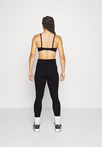 Un reggiseno sportivo nero e leggings a vita alta indossati da una persona, che mostrano una texture liscia e un design aderente. Il reggiseno ha spalline regolabili; i leggings sono lunghi fino alla caviglia.