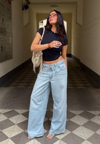 Jeans large bleu clair avec taille à cordon, associés à un t-shirt noir court. Les accessoires comprennent un sac clair et des bagues en argent.
