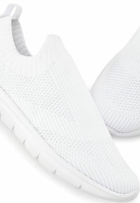 White slip-on sneakers made of knitted fabric with a textured pattern. Features a flexible sole and ribbed ankle for a secure fit.