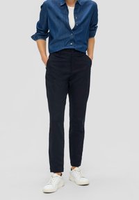 Navy kalhoty s tapered střihem, plochým předním dílem a bočními kapsami. Spárovány s džínovou košile a bílými teniskami na neutrálním pozadí.