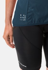 T-skjorte med korte ermer i mørk blå farge for sykling, med "RECYKLET INNI" trykk, kombinert med svarte stretchshorts med buet sømdetalj og logo.