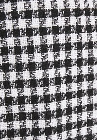 Mustavalkoinen ruudullinen kangas, jossa on saumaton kudontatekniikka, esittää vuorotellen erilaisia kokoja olevia neliöitä, luoden klassisen kuvion.