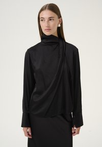 Sort satin top med høj krave, draperet front og lange ærmer. Har knaplukning ved ærmerne og en glat, blank tekstur.