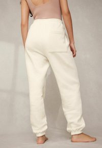Helle Sweatpants in Creme mit elastischen Bündchen und einer einzigen Gesäßtasche, aus weichem Material für Komfort und eine lockere Passform gefertigt.