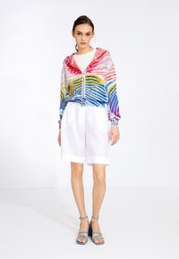 Colorful hooded jacket with vibrant striped pattern in blue, pink, yellow. Paired with white shorts and blue strappy sandals.