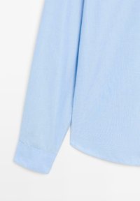 Lichtblauwe lange mouwen shirt met een soepele textuur, voorzien van een afgeronde zoom en een knoopmanchet. Het materiaal lijkt ademend en lichtgewicht.