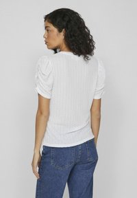 Haut blanc texturé avec des manches courtes bouffantes, silhouette ajustée et encolure ronde, associé à un jean bleu foncé.