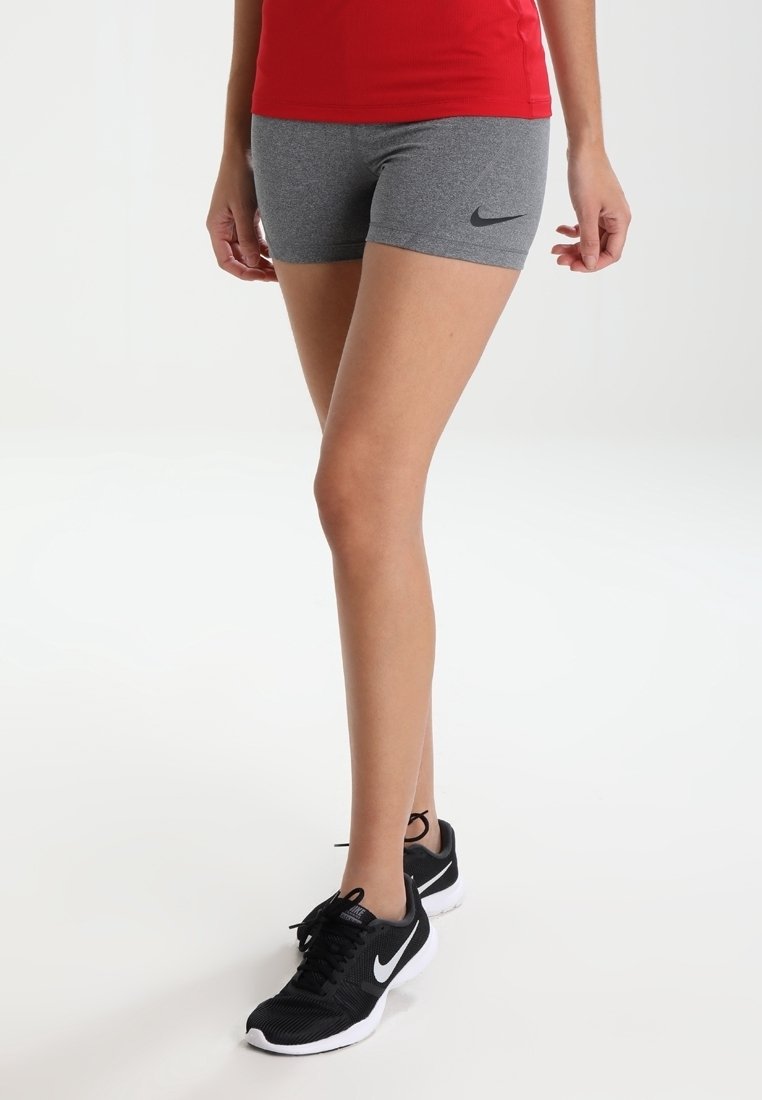 Szare krótkie spodenki sportowe z czarnym logo Nike, w zestawieniu z czarnymi sneakersami z białymi akcentami. Gładka tkanina, dopasowany krój i minimalistyczny styl.