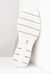 Semelle d'une chaussure de sport avec un design en caoutchouc blanc texturé et des rainures parallèles, complétée par un dessus beige clair et un détail de marque subtil.