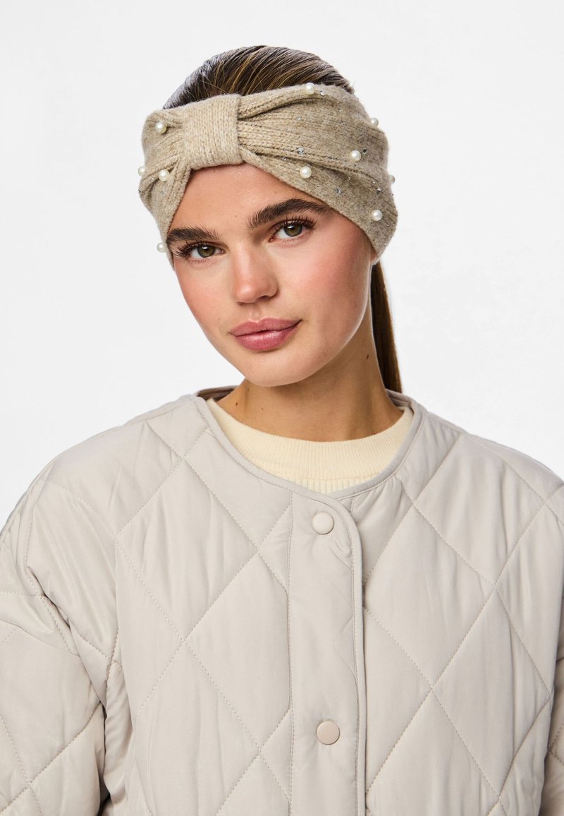 Beidzis adīts galvas variants ar mezglu dizainu, rotāts ar pērlēm un mazām dārgakmeņiem, kopā ar vieglu quilt jacket.