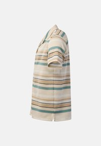Chemise en maille à manches courtes avec col, présentant des rayures horizontales beige, bleu sarcelle, noir et blanc, vue de profil sur fond uni.