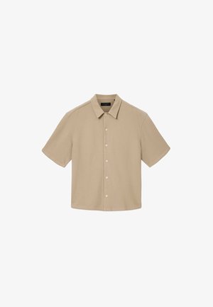 Camicia beige a maniche corte realizzata in tessuto morbido, con chiusura frontale a bottoni e colletto classico. Texture liscia con design semplice e senza motivi.