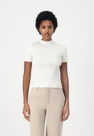 Lys ribbestrikket topp i off-white med høy, volanghals og korte ermer, kombinert med beige skræddersydde bukser.