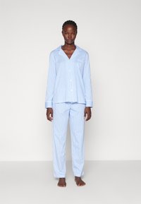 Modra in bela prugasta pižama, ki vključuje dolge rokave, usklajene hlače in žep na prsih. Tkanina se zdi gladka in lahka.