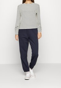 Pasiasta koszula z długim rękawem w kolorze kremowym i granatowym, zestawiona z granatowymi spodniami dresowymi. Mieszanka bawełny, luźny krój, elastyczne mankiety i pas.