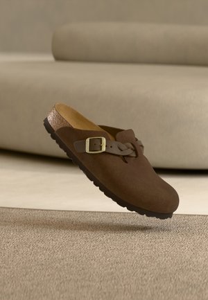 Pantof maro din piele întoarsă tip slip-on, cu o curea împletită și o cataramă metalică, având o talpă conturată și o talpă exterioară texturată din cauciuc.