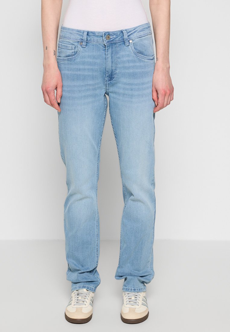 Hellblaue Denim-Jeans mit geradem Schnitt, Fünf-Taschen-Design, ausgewaschenem Look und metallischem Knopfverschluss, kombiniert mit beigen Sneakers.