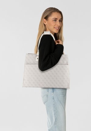 Bolso tote blanco con un patrón de logotipo en relieve, forma estructurada, asas resistentes, textura suave y un atuendo negro en contraste que lleva puesto el modelo.