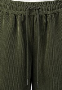Green corduroy pants with vertical ribbing, featuring an elastic waistband and adjustable drawstring. Silver hardware accents on drawstring ends.