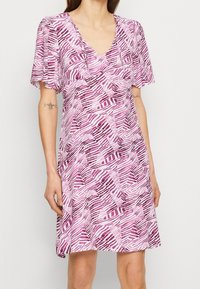 Klänning med V-ringning som har ett geometriskt mönster i olika nyanser av rosa, med korta, löst sittande ärmar och ett lätt tyg.