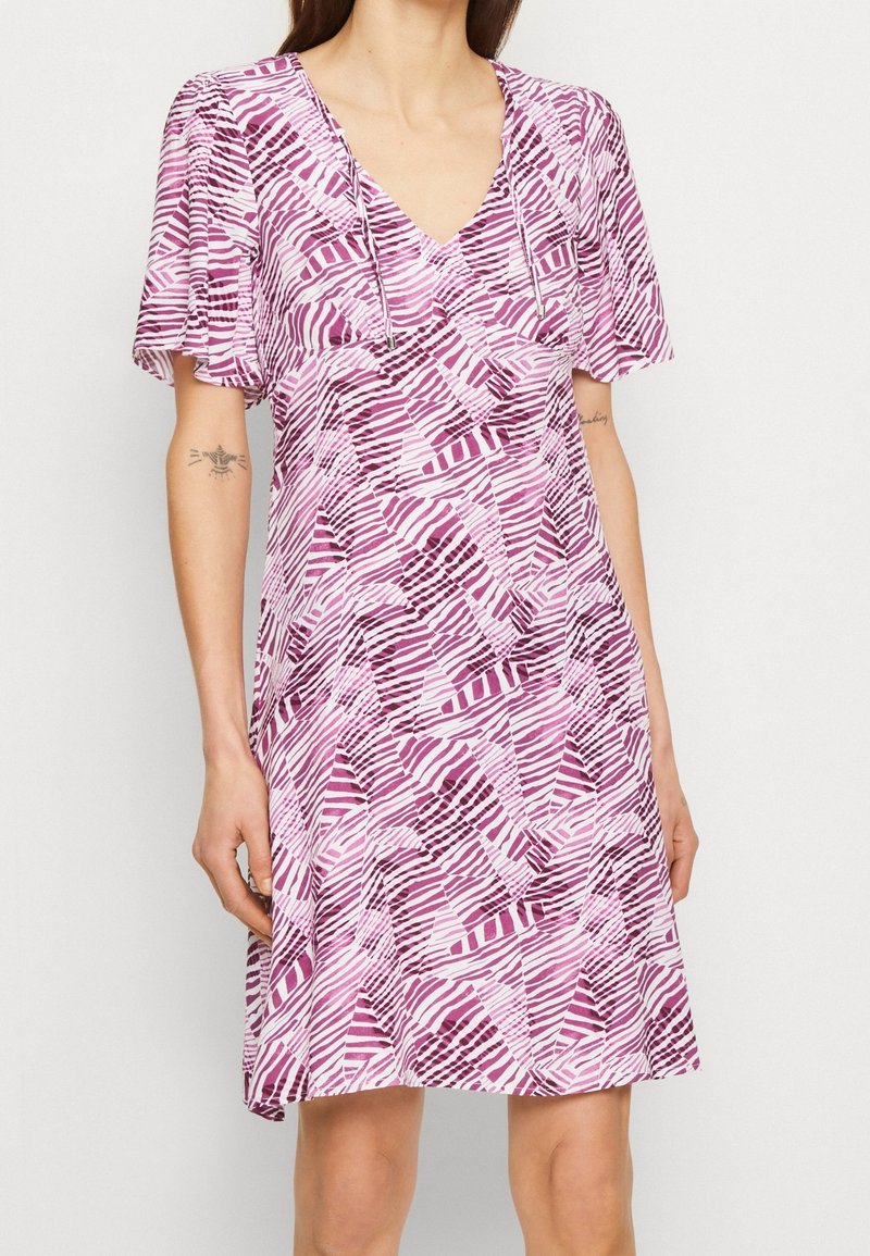 Klänning med V-ringning som har ett geometriskt mönster i olika nyanser av rosa, med korta, löst sittande ärmar och ett lätt tyg.