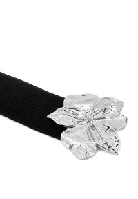 Cintura elastica nera con una grande fibbia a forma di fiore in metallo argentato, dotata di petali texturizzati e una finitura lucida.