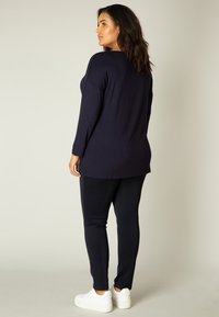 Marineblauw langemouwtop met een relaxte pasvorm, gecombineerd met zwarte slim-fit broek en witte sneakers; gladde stof met een eenvoudig ontwerp.