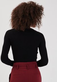 Haut noir à manches longues côtelé associé à un pantalon bordeaux taille haute. Le haut présente une silhouette ajustée et un col rond.