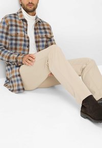 Camicia a quadri nelle tonalità di marrone, blu e crema, abbinata a pantaloni beige e stivali in pelle scura. Tessuto morbido, vestibilità rilassata.