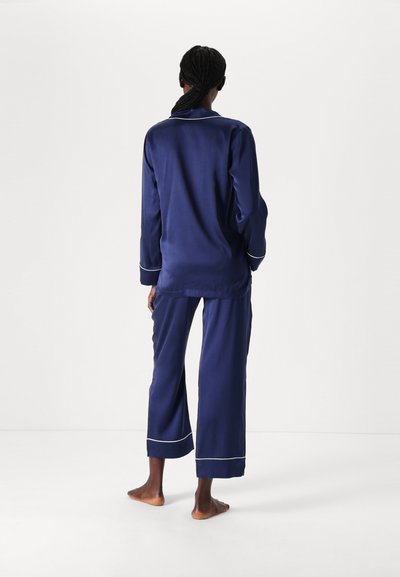 Navy Satin-Schlafanzug-Set mit langen Ärmeln, lockerer Passform bei den Hosen, weißen Paspelierungen und einem entspannten Design.
