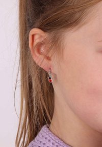 Zilveren lieveheersbeestje oorknopjes hebben een rood en zwart ontwerp, hangend aan kleine zilveren studs. Haar bedekt gedeeltelijk het oor.
