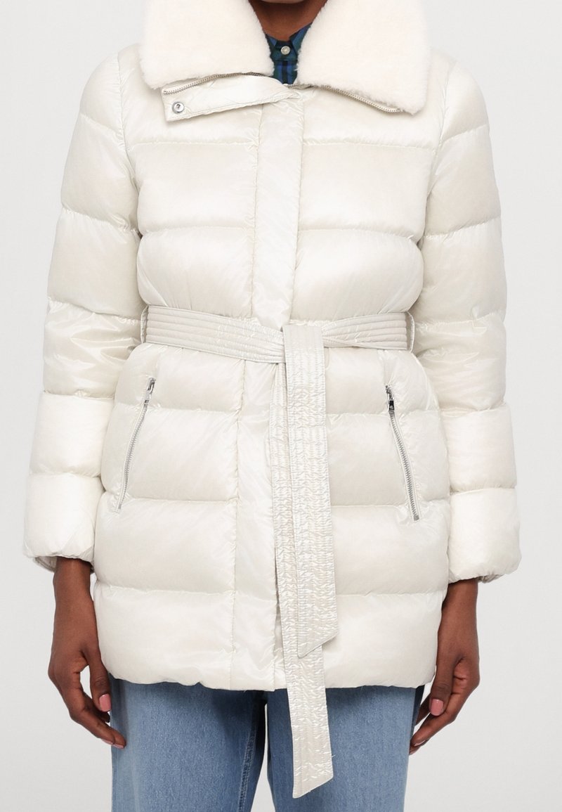 Puffer coat in light cream, featuring a fur collar, belted waist, and zippered pockets, with quilted design and smooth texture.
